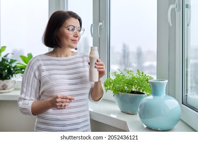 Middle-aged Woman Drinking Milk Drink, Liquid Yogurt In Bottle, At Home Near Window