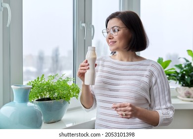 Middle-aged Woman Drinking Milk Drink, Liquid Yogurt In Bottle, At Home Near Window
