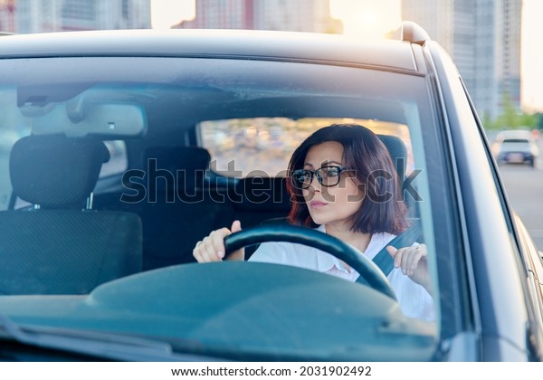 Middle-aged woman driver with glasses, female\
driving a car.