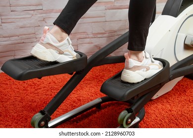 A middle-aged woman is exercising at home on an elliptical trainer. - Powered by Shutterstock