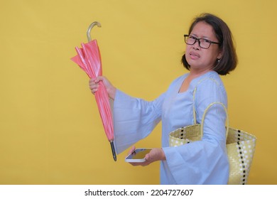 A Middle-aged Woman With A Handbag On Her Shoulder, One Hand Holding A Cell Phone, The Other Hand Holding An Umbrella; Irritated Expression