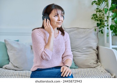 Middle-aged woman in headphones listening to audio, music, audiobook, communication - Powered by Shutterstock