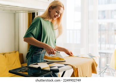 Middle-aged woman housewife ironing clothes at home.
