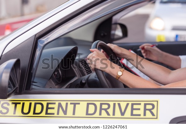 Middle-aged woman learning to drive a car with\
a driving\
instructor