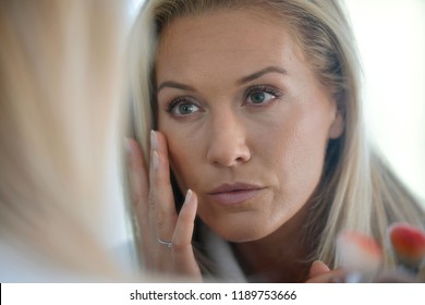 Middle-aged woman looking at her skin in front of mirror