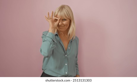 Middle-aged woman making an ok gesture in front of her eye while standing against an isolated pink background. - Powered by Shutterstock