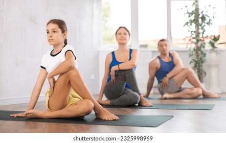 Middle-aged woman, man, teenage girl and boy practicing Lord of the Fishes Pose, or Matsyendrasana on mats during family Hatha yoga class in wellness studio - Powered by Shutterstock