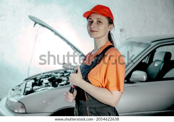 Middle-aged woman mechanic with a wrench in the\
front open hood of the car. Female Vehicle fitter inspecting a used\
car. Car components, labor open hood of the car. Service center,\
auto repair shop