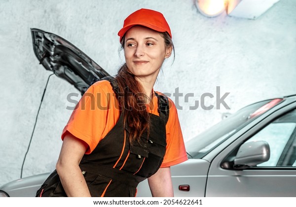 Middle-aged woman mechanic with a wrench in the\
front open hood of the car. Female Vehicle fitter inspecting a used\
car. Car components, labor open hood of the car. Service center,\
auto repair shop