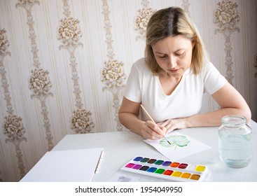 A middle-aged woman paints on paper. Drawing monstera leaf in watercolor. The woman is engaged in her hobby. Drawing hobby for a woman. - Powered by Shutterstock