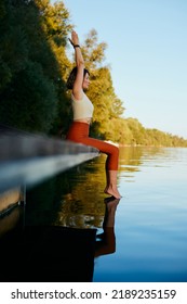 A Middle-aged Woman Is Relaxing On The Dock And Doing Yoga Breathing Exercises. She Put Her Feet In The Water.