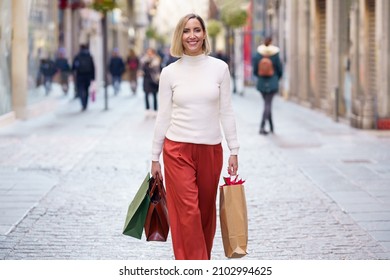 Middle-aged woman shopping in a shopping street carrying bags with what she has bought. - Shutterstock ID 2102994625