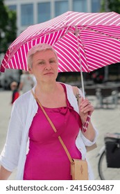 middle-aged woman with a short haircut with an umbrella protecting from the scorching sun is looking for something in her handbag, and smile, High quality photo