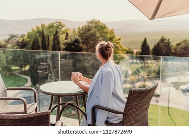 A middle-aged woman sits in a street cafe overlooking the mountains at sunset. She is dressed in a blue jacket and drinks coffee admiring the nature. Travel and vacation concept. - Shutterstock ID 2127872690