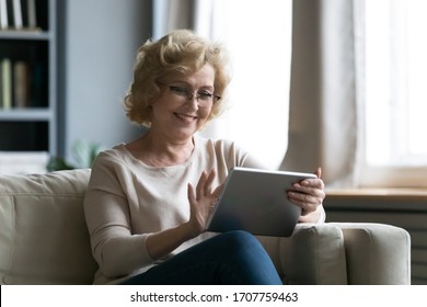 Middle-aged woman sitting on sofa in living room having fun using tablet smiling enjoy distant chat with grown up children or friend older generation and modern technology easy usage of device concept - Powered by Shutterstock