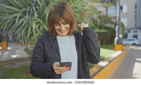 A middle-aged woman smiles while using a smartphone outdoors in casual attire, exuding joy and modern connectivity.