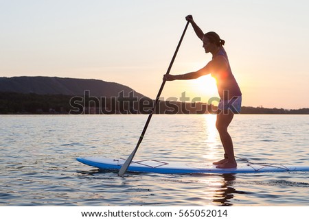 A middle-aged woman stand up paddle boards on a bay at sunset in Ontario, Canada.