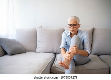 Middle-aged woman suffering from pain in leg at home, closeup. Physical injury concept. Ankle pain, painful point. Problems with feet, joints, legs and ankles. 