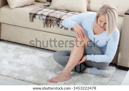 Middle-aged woman suffering from pain in leg at home, closeup. Physical injury concept. Ankle pain, painful point.