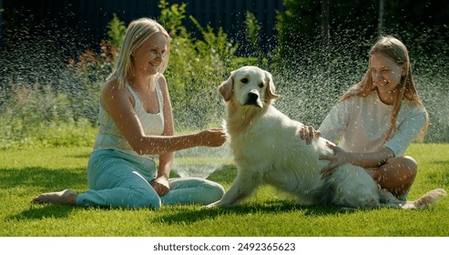 A middle-aged woman and a teenager play with a Golden Retriever in the yard, enjoying the sprinkler refreshing spray on a sunny day. - Powered by Shutterstock