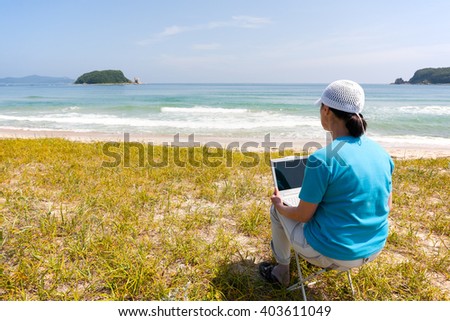 Middle-aged woman uses a personal computer while on the beach on a summer day