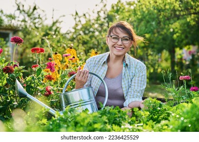 Middle-aged woman with watering can near garden bed with spicy fragrant herbs - Powered by Shutterstock