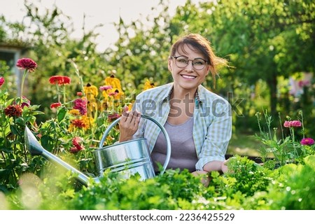 Middle-aged woman with watering can near garden bed with spicy fragrant herbs