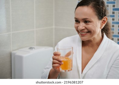 Middle-aged Woman In White Bathrobe Holding A Glass Of Pure Water With Effervescent Tablet, Smiling A Toothy Smile, Taking Daily Dose Of Vitamins, Minerals And Dietary Nutritional Supplement