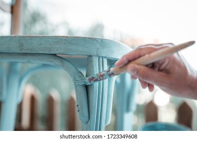 Middle-aged woman's hand with brush restores a wooden chair with turquoise paint - Shutterstock ID 1723349608