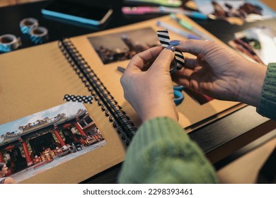 Middle-aged woman's hands holding a roll of washi tape that she is going to use to paste a photo onto her handmade kraft travel album. The sign says the word temple in Thai languaje.