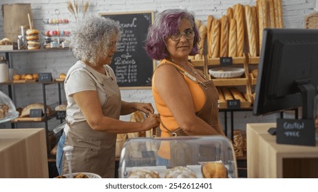 Middle-aged women working together in a cozy bakery, one assisting the other with her apron in an inviting indoor setting full of bread and pastries - Powered by Shutterstock