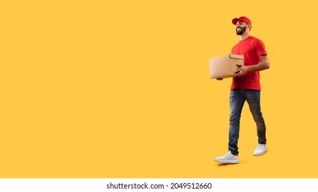 Middle-Eastern Courier Man Carrying Cardboard Box Delivering Package Looking Aside At Copy Space Posing Over Yellow Studio Background. Delivery Service. Full Length Shot - Shutterstock ID 2049512660