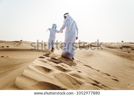 Middle-eastern father and son wearing arab traditional kandura spending time in the desert, Dubai