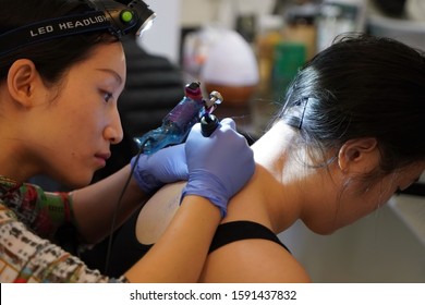 Middletown, CT / USA - December 7, 2019: Asian Tattoo Artist Concentrates While Tracing A Floral Tattoo Design On The Back Of The Client's Neck