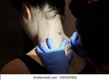 Middletown, CT / USA - December 7, 2019: Asian Tattoo Artist Concentrates While Tracing A Floral Tattoo Design On The Back Of The Client's Neck