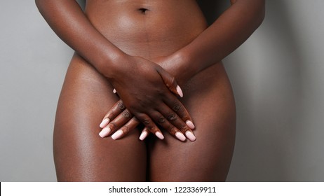 midesction of unrecognizable naked african woman covering genital area with her hands - female sexuality or gynecology or women's health concept