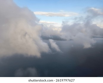 Mid-flight image showing massive clouds with a blue backdrop, revealing small patches of land below.