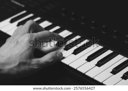 A midi keyboard with a man's hand playing it, piano keys.