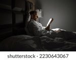 Midle-aged caucasian man relaxing in bed reading bestseller novel paper book with bedside lamp turned on. Evening relaxation, hobbies, free time concept. Adulthood concept.