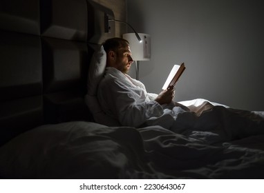 Midle-aged caucasian man relaxing in bed reading bestseller novel paper book with bedside lamp turned on. Evening relaxation, hobbies, free time concept. Adulthood concept. - Powered by Shutterstock