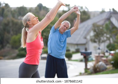 Mid-length Shot Of An Active Senior Couple In Sportswear Warming Up On The Driveway Stretching Arms Above Head.