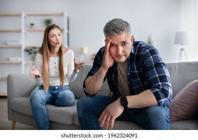 Midlife crisis and family conflicts. Mature man holding his head in stress, having fight with his angry wife at home, copy space. Middle-aged married couple going through divorce or breakup - Powered by Shutterstock