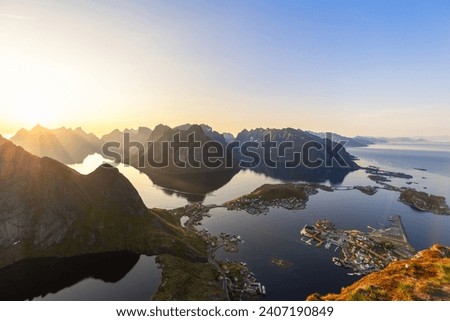Midnight sun softly dips towards the horizon, a breathtaking view from Reinebringen unfolds, with sharp mountain ridges and the calm waters of the Norwegian Sea in the Lofoten archipelago
