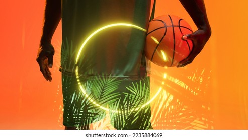 Midsection of african american basketball player holding ball by illuminated circle and plants. Copy space, composite, hand, sport, competition, illustration, illuminated, nature, shape and abstract. - Powered by Shutterstock
