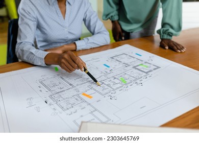 Midsection of african american female architects analyzing blueprint on desk in office, copy space. Unaltered, architecture, construction industry, design, teamwork, paper, hand and business concept. - Powered by Shutterstock