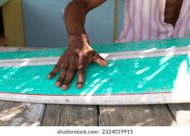 Midsection of african american man preparing surfboard behind counter of surf hire beach shack. Local business, business owner, hobbies, sport, surfing, summer and vacation. - Powered by Shutterstock