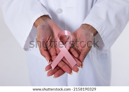 Midsection of african american mid adult female doctor with pink breast cancer awareness ribbon. hand, breast, cancer, doctor, medical, ribbon, awareness, support, healthcare and hospital concept.
