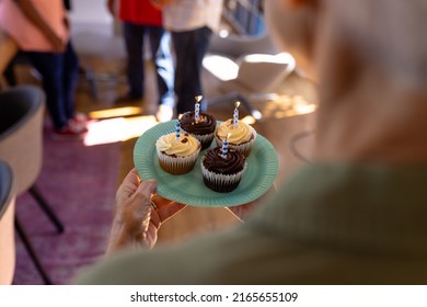 Midsection Of Asian Senior Woman Holding Plate With Cupcakes And Candles In Nursing Home. Birthday, Celebration, Party, Sweet Food, Enjoyment, Unaltered, Support, Assisted Living And Retirement.