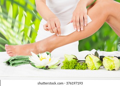 Midsection Of Beautician Waxing Woman's Leg With Wax Strip At Beauty Spa