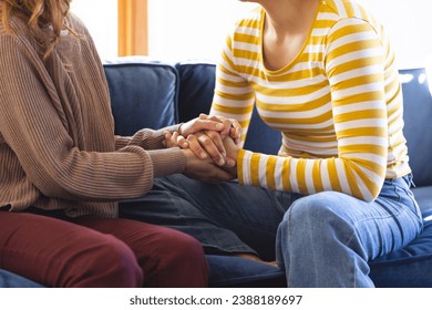 Midsection of biracial lesbian couple holding hands sitting on couch at home. Gay, love, relationship, togetherness, domestic life and lifestyle, unaltered. - Powered by Shutterstock